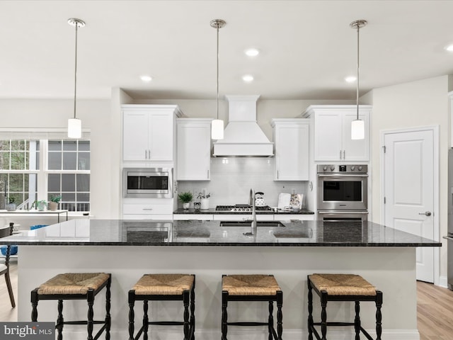 kitchen with a center island with sink, light hardwood / wood-style flooring, stainless steel appliances, and custom exhaust hood