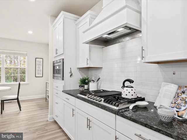 kitchen with appliances with stainless steel finishes, light wood-type flooring, dark stone counters, custom exhaust hood, and white cabinetry