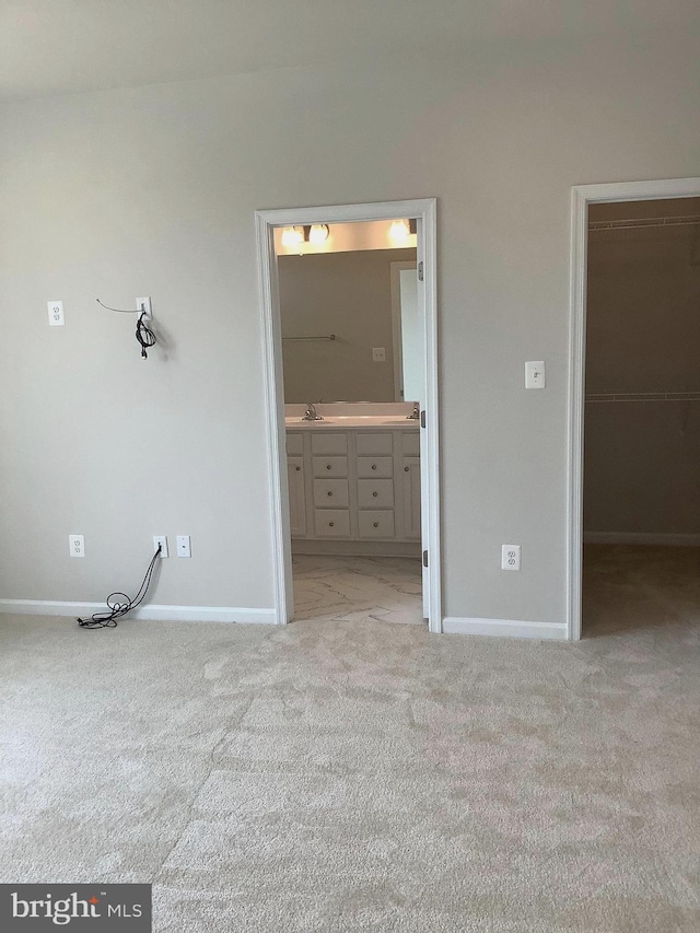 unfurnished bedroom with ensuite bath, light colored carpet, sink, a spacious closet, and a closet