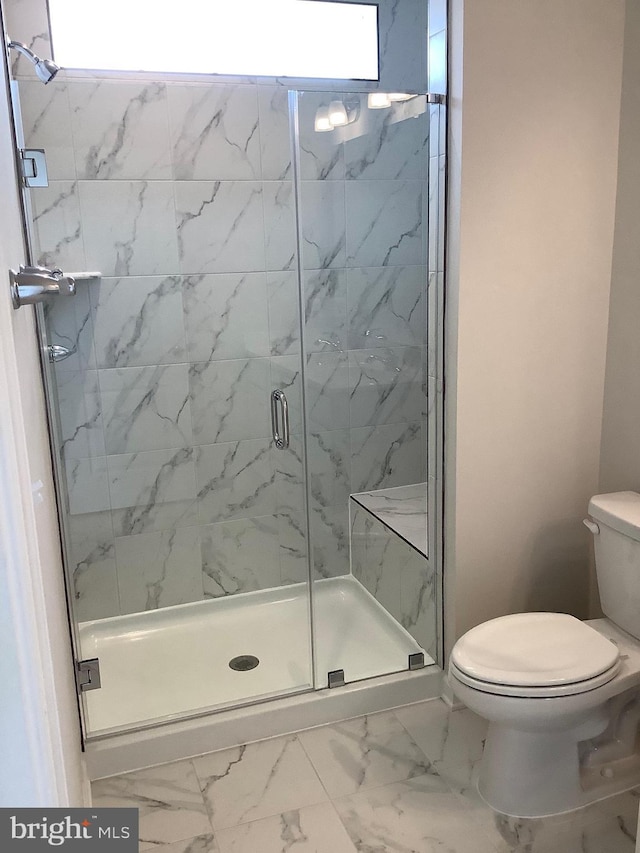 bathroom featuring a shower with door and toilet