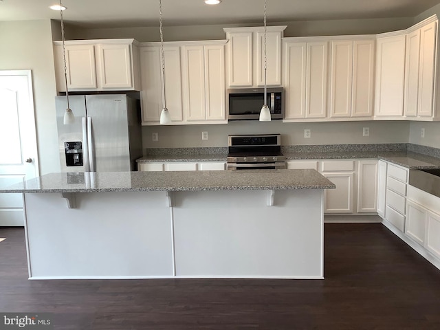 kitchen featuring appliances with stainless steel finishes, a center island, dark hardwood / wood-style flooring, and pendant lighting