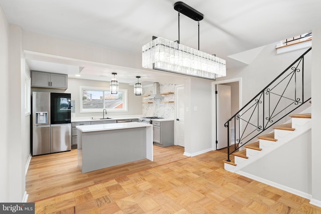 kitchen with gray cabinetry, a center island, wall chimney range hood, stainless steel refrigerator with ice dispenser, and decorative light fixtures