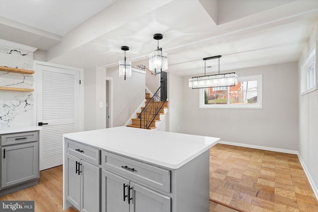 kitchen featuring gray cabinetry, a notable chandelier, a center island, decorative light fixtures, and light parquet flooring