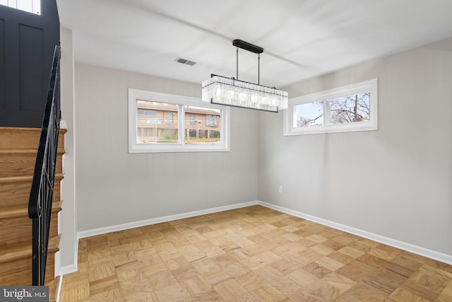 unfurnished dining area featuring a healthy amount of sunlight, an inviting chandelier, and light parquet flooring