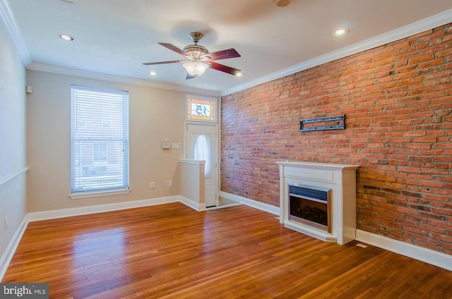 unfurnished living room featuring hardwood / wood-style floors, ceiling fan, crown molding, and brick wall