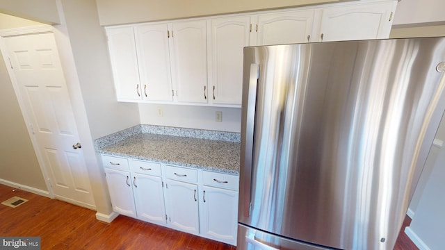 kitchen featuring white cabinets, stainless steel fridge, dark hardwood / wood-style flooring, and light stone counters