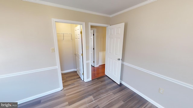 unfurnished bedroom with a walk in closet, dark hardwood / wood-style flooring, ornamental molding, and a closet