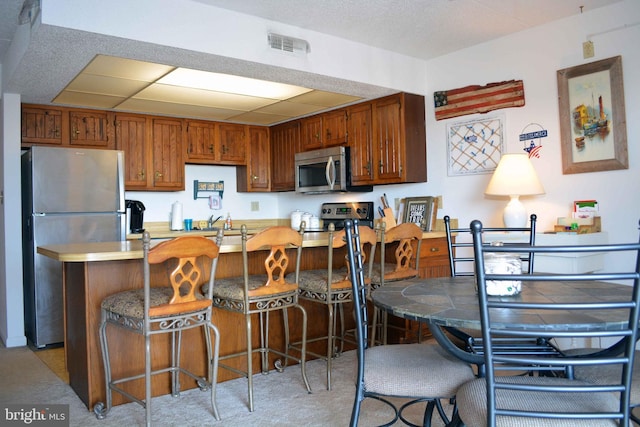 kitchen featuring brown cabinets, stainless steel appliances, light countertops, a peninsula, and a kitchen breakfast bar