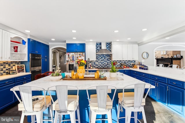 kitchen featuring blue cabinetry, appliances with stainless steel finishes, tasteful backsplash, and wall chimney exhaust hood