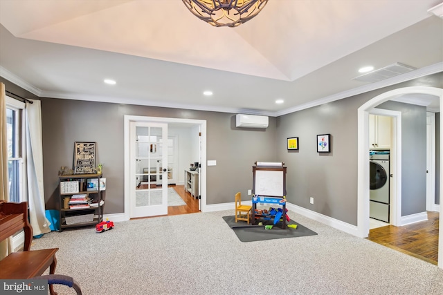 recreation room with a wall unit AC, washer / clothes dryer, light colored carpet, and ornamental molding