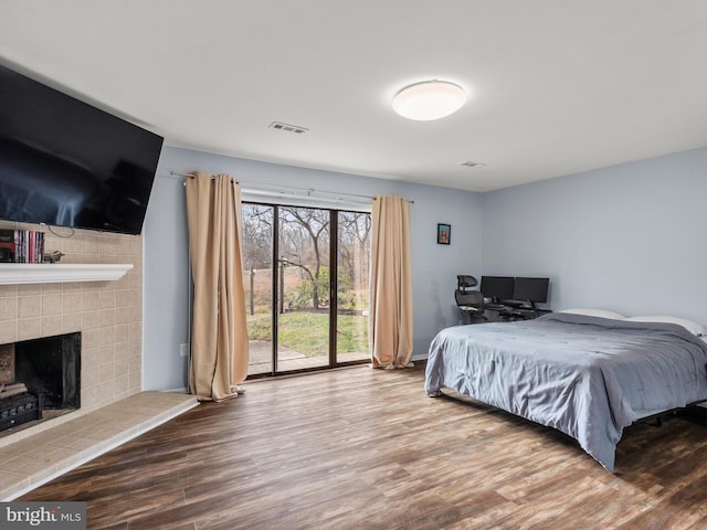 bedroom featuring hardwood / wood-style flooring, a tile fireplace, and access to outside