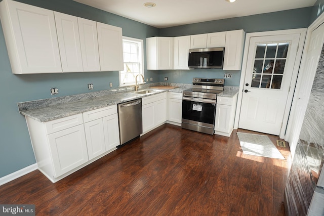 kitchen featuring appliances with stainless steel finishes, light stone counters, dark wood-type flooring, sink, and white cabinetry