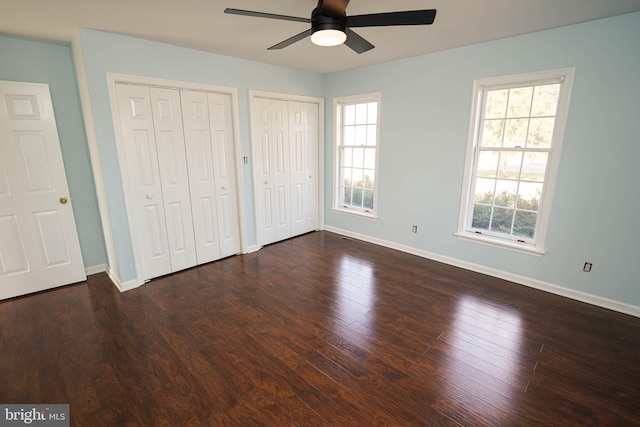 unfurnished bedroom featuring multiple closets, ceiling fan, and dark hardwood / wood-style flooring