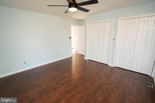 unfurnished bedroom featuring ceiling fan, dark hardwood / wood-style flooring, and multiple closets