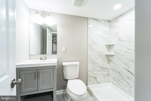 bathroom with a tile shower, vanity, and toilet