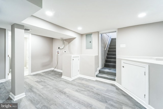 basement featuring electric panel and light hardwood / wood-style flooring