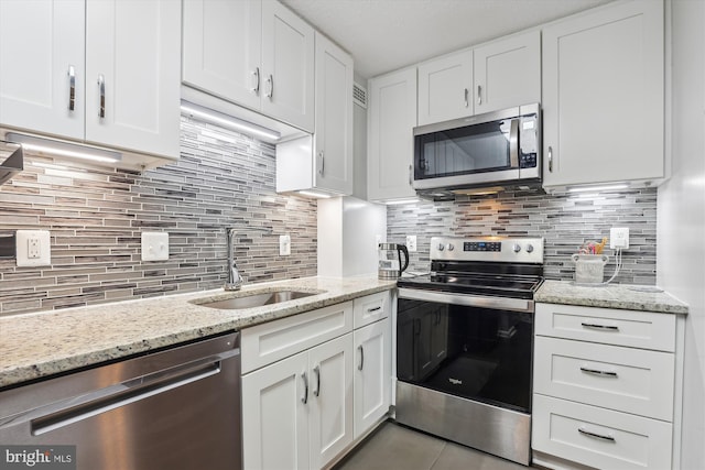 kitchen with tasteful backsplash, light stone counters, stainless steel appliances, sink, and white cabinetry