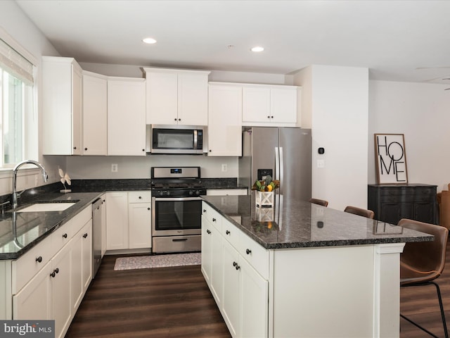 kitchen featuring sink, stainless steel appliances, dark stone counters, a breakfast bar area, and white cabinets