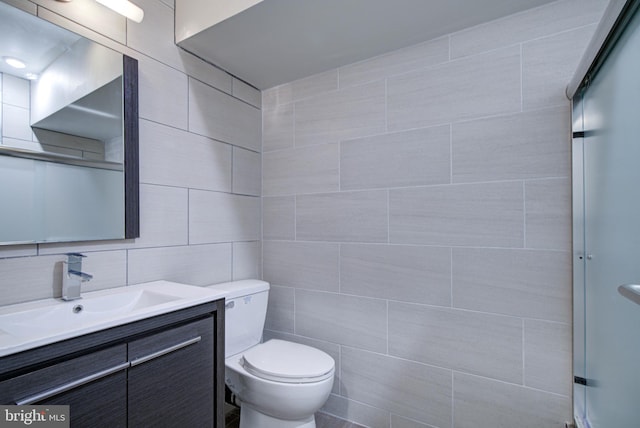 bathroom with a shower with door, vanity, tile walls, and toilet