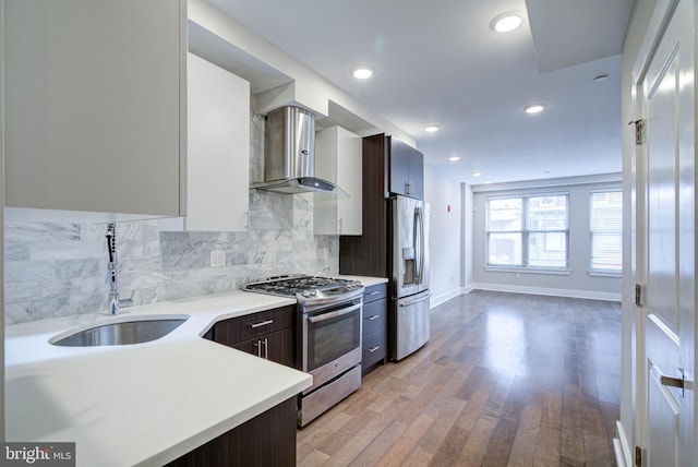 kitchen featuring wall chimney range hood, sink, light wood-type flooring, dark brown cabinetry, and stainless steel appliances