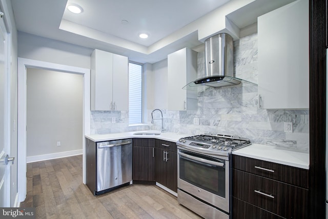 kitchen featuring appliances with stainless steel finishes, wall chimney exhaust hood, dark brown cabinets, sink, and white cabinets