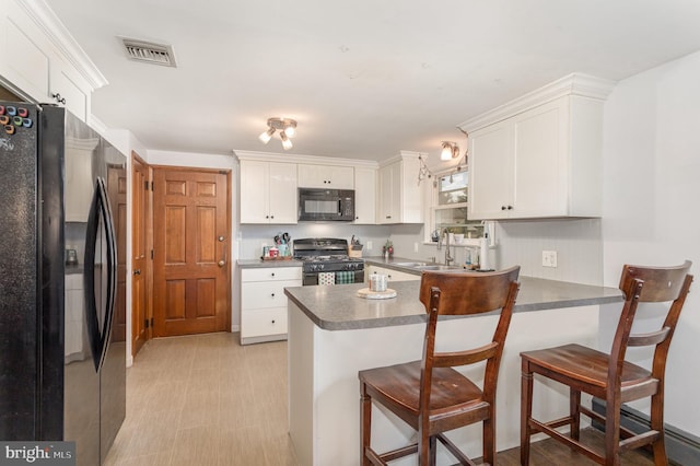 kitchen with kitchen peninsula, sink, white cabinetry, and black appliances