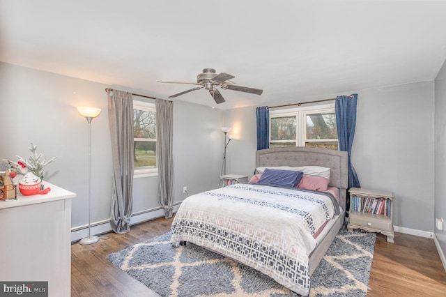 bedroom with ceiling fan, a baseboard heating unit, wood-type flooring, and multiple windows