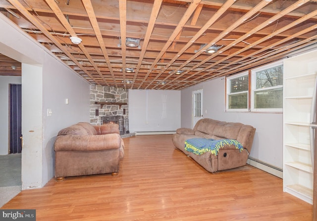 sitting room with baseboard heating, a stone fireplace, and light wood-type flooring