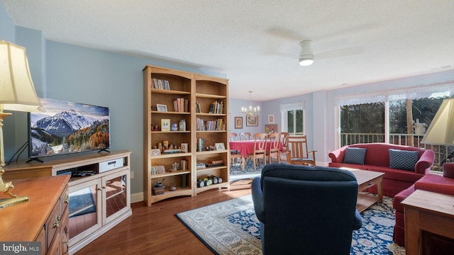 living room featuring dark hardwood / wood-style flooring, ceiling fan with notable chandelier, and a textured ceiling