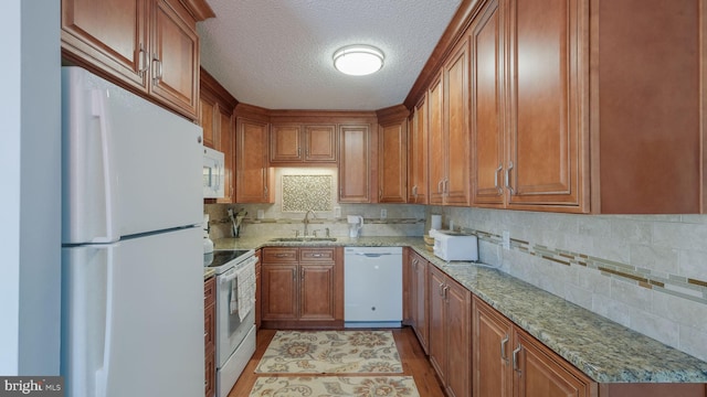 kitchen featuring light wood-type flooring, white appliances, light stone counters, and sink