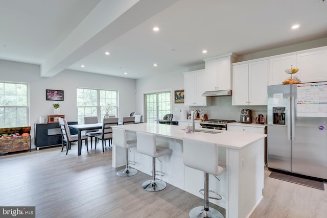 kitchen featuring stainless steel refrigerator with ice dispenser, a breakfast bar area, a center island with sink, white cabinets, and backsplash