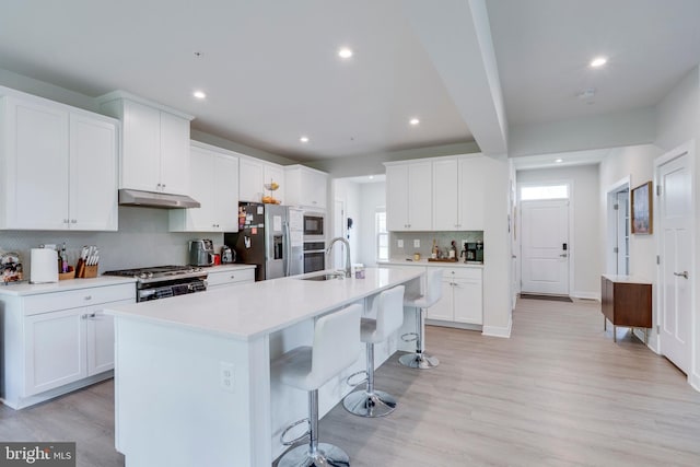 kitchen featuring a kitchen bar, sink, white cabinetry, appliances with stainless steel finishes, and a kitchen island with sink