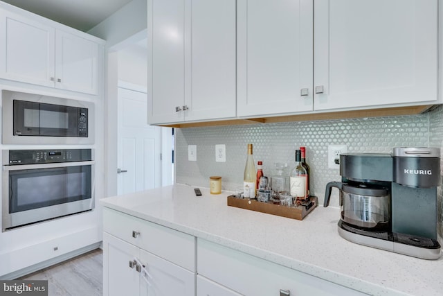 kitchen featuring black microwave, light stone counters, oven, and white cabinets