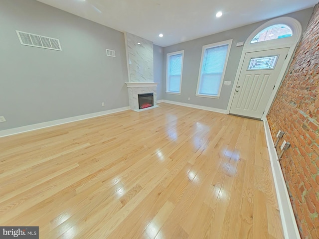 unfurnished living room with brick wall, light wood-type flooring, and a high end fireplace