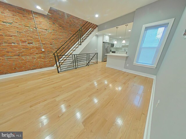 unfurnished living room featuring light hardwood / wood-style flooring, a towering ceiling, and brick wall