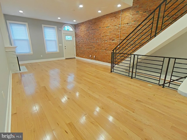 foyer with a towering ceiling, light wood-type flooring, and brick wall