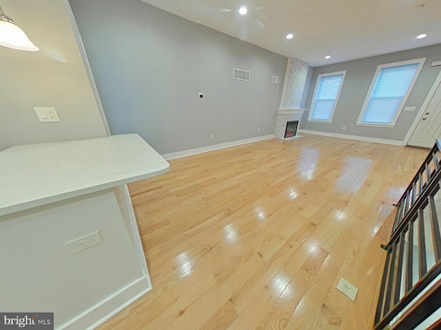 unfurnished living room with ceiling fan, a large fireplace, and light hardwood / wood-style flooring