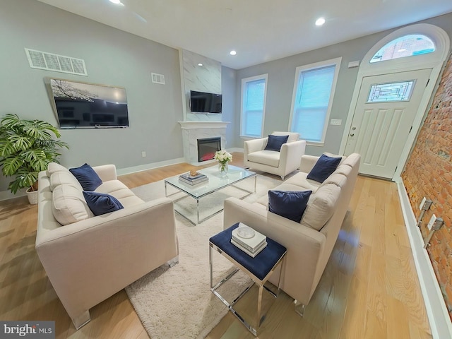 living room with brick wall, light wood-type flooring, and a premium fireplace