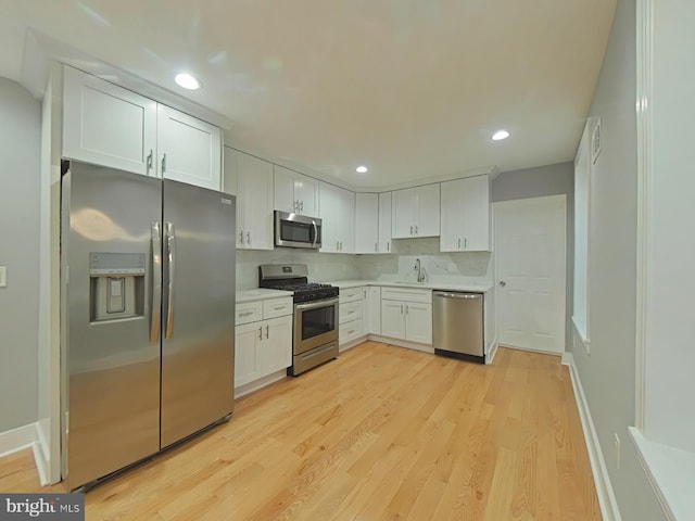 kitchen with white cabinetry, sink, stainless steel appliances, light hardwood / wood-style floors, and decorative backsplash