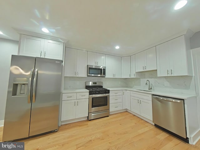 kitchen with decorative backsplash, appliances with stainless steel finishes, light wood-type flooring, sink, and white cabinetry