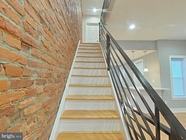 stairway with wood-type flooring and brick wall