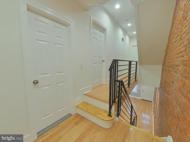 staircase with hardwood / wood-style floors and brick wall