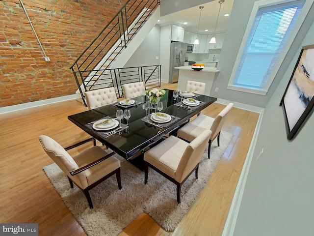 dining room featuring brick ceiling, light hardwood / wood-style flooring, brick wall, and a high ceiling