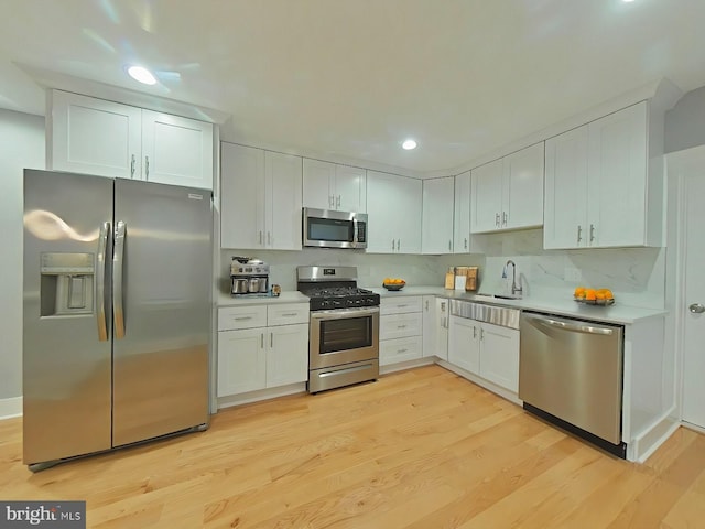 kitchen featuring decorative backsplash, appliances with stainless steel finishes, sink, light hardwood / wood-style flooring, and white cabinets