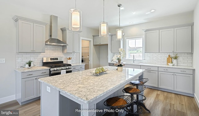 kitchen with a center island, stainless steel range with gas cooktop, sink, wall chimney range hood, and decorative light fixtures