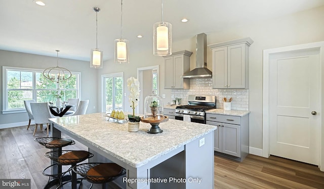 kitchen featuring wall chimney range hood, hardwood / wood-style flooring, stainless steel gas stove, gray cabinets, and hanging light fixtures