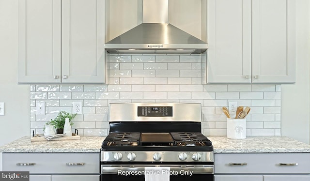 kitchen with backsplash, light stone countertops, stainless steel gas stove, and wall chimney range hood