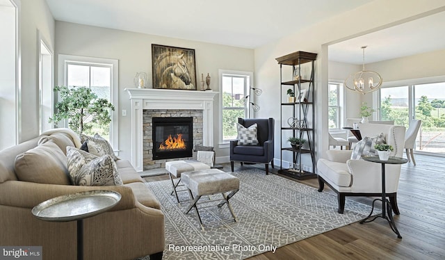 living room featuring plenty of natural light, a stone fireplace, wood-type flooring, and an inviting chandelier