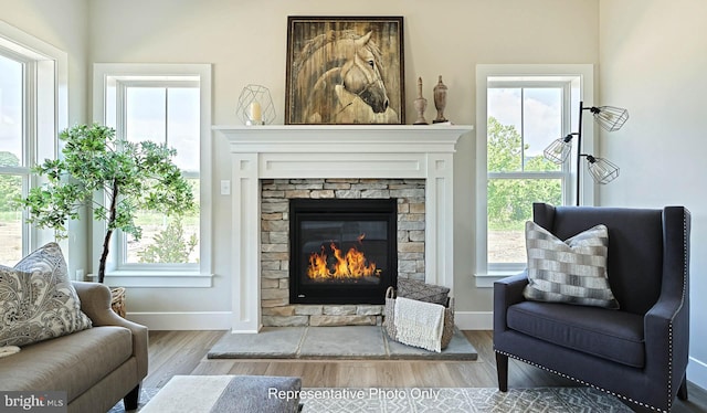 living area featuring light wood-type flooring, a stone fireplace, and plenty of natural light