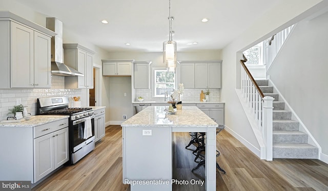 kitchen featuring wall chimney exhaust hood, a wealth of natural light, a kitchen island, and appliances with stainless steel finishes